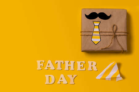 Gift box on a yellow background with the inscription in wooden letters Father's Day. Flat lay. Father's day gift to dad. Happy Father's Day holiday concept in 2021. Copy spaceの写真素材
