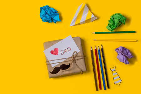 Gift box with a note love you dad on a yellow background with pencils and paper with copy space. Flat lay. Child's gift to dad for father's day. Happy father's day holiday concept.の写真素材