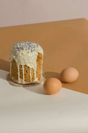Two brown chicken eggs and traditional exquisite Easter cake on trendy isometric beige background....