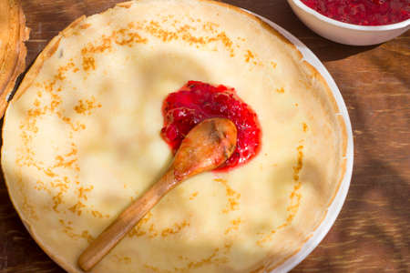 Spoon with red currant jam on a thin pancake. Traditional Russian food.