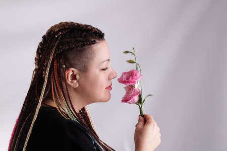 Portrait of cute young woman with braided pigtails sniffing flower.