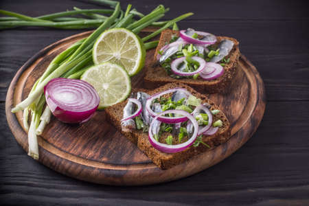Black bread sandwiches with cut salted Black Sea sprat carcasses with onions and parsley on a round wooden boardの写真素材