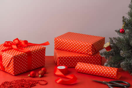 Red wrapping paper, ribbons, scissors and gift boxes on the table near the wall. Christmas gift wrapping conceptの写真素材