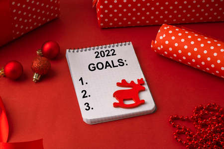 Goals for 2022 on a blank sheet of paper, among Christmas gifts on a red background. Concept of the upcoming christmas holidaysの写真素材