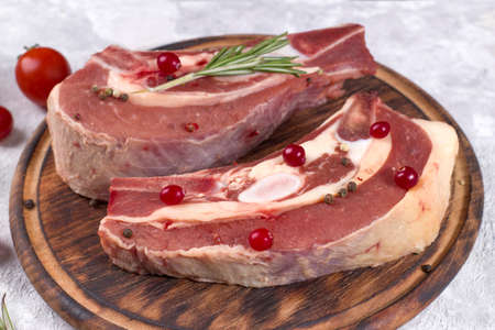 Several pieces of raw beef brisket on the bone with cranberries, rosemary and cherry tomatoes on a light backgroundの写真素材