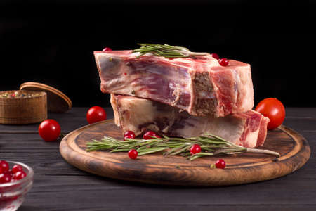 Several pieces of raw beef brisket on the bone with cranberries, rosemary and cherry tomatoes on a dark wooden backgroundの写真素材