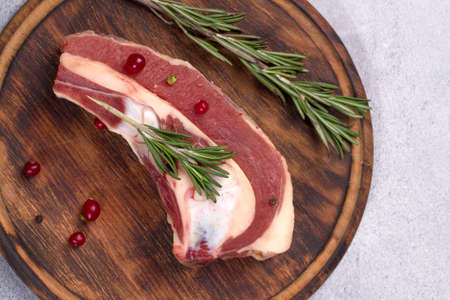 Piece of fresh raw beef brisket on the bone with cranberries and rosemary on a wooden round board on a light background. Top view.の写真素材