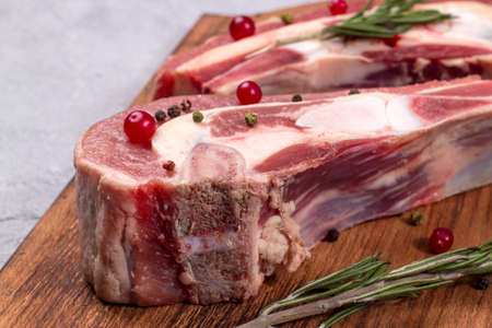 Slice of fresh raw beef brisket on the bone with cranberries and rosemary on a wooden board. Close up.の写真素材