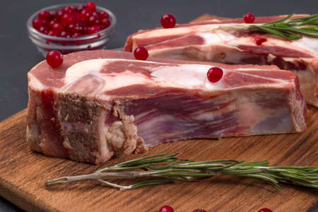 Several pieces of fresh raw beef brisket on the bone with cranberries and rosemary on a wooden boardの写真素材