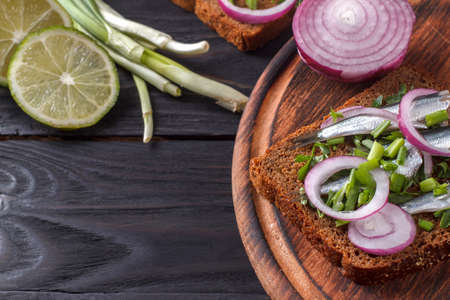 Black bread sandwiches with cut salted Black Sea sprat carcasses with onions and parsley a wooden boardの写真素材