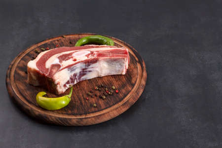 Piece of fresh raw beef brisket on the bone with chili and peppercorns on a wooden board on a dark background with copy spaceの写真素材
