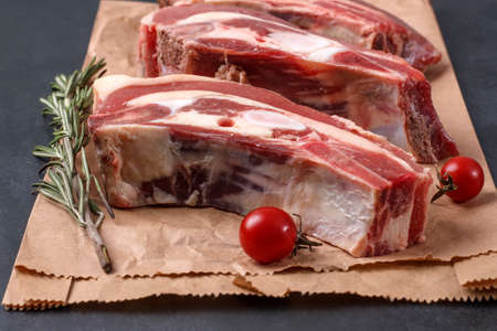 Several pieces of fresh raw beef brisket on the bone with cherry tomatoes and rosemary on wrapping paperの写真素材