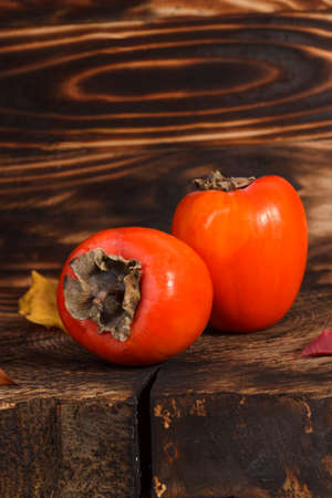 Fresh orange persimmon fruits on wooden table with autumn leaves.の写真素材