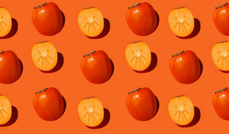 Fresh fruit and berry seamless pattern. Ripe persimmons. Autumn pattern is made with half a persimmon on a bright light orange background. Minimal autumn concept. Monochrome banner.の写真素材