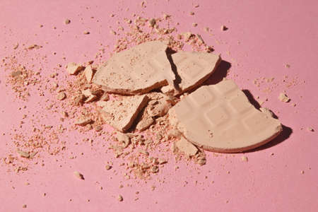 Face powder. Broken pieces of cosmetic powder on a pink background with a hard shadow. Cosmetic smear.の写真素材