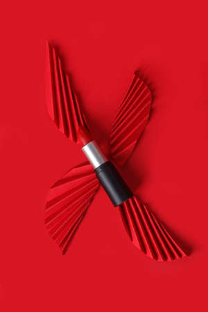 Red lipstick with paper craft on red background. Creative concept of trendy flat lay photo of cosmeticsの写真素材