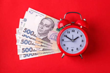 Time is money. Red alarm clock on several Ukrainian 500 hryvnia bills on a red background.の写真素材