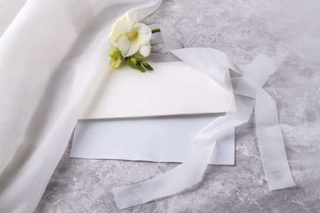 Wedding blank and an envelope with a delicate freesia flower on a light table. Top view with copy space. Template for branding and advertisingの写真素材