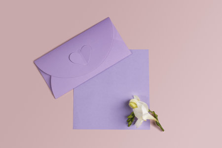 Wedding invitation mockup with an very peri envelope, a sheet of paper and a delicate freesia flower on pink background. Template for branding and advertisingの写真素材