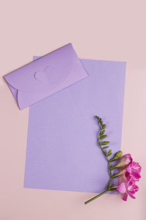 Flat lay with empty greeting card with very peri envelope and freesia flower on pink background, top view, copy space. Template for branding and advertisingの写真素材
