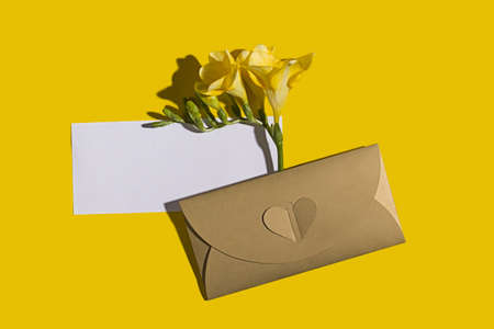 Stylish wedding invitation mockup with golden envelope and freesia flower on yellow background with...