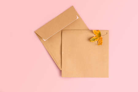Invitation or greeting card mockup with craft envelopes on soft pink background with autumn leaf.