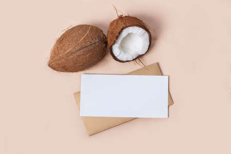 Coconut and an empty blank with an envelope on a sandy background. Summer still life with...