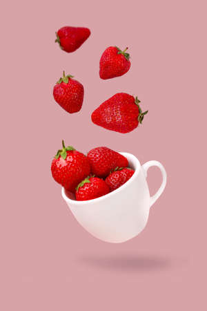 Juicy strawberries fly into a cup on a pastel pink background.Food levitation or zero gravity conceptionの写真素材