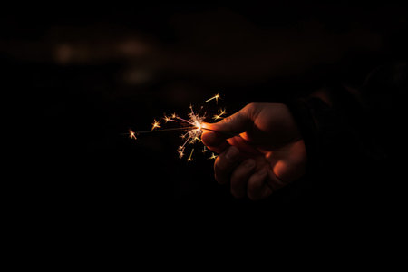 Hand Holding Sparkler in Dark Background Celebrating Night Event with Bright Lightの素材