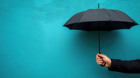 Hand Holding Black Umbrella Against Bright Blue Wall Background Minimalist Conceptual Photographyの素材