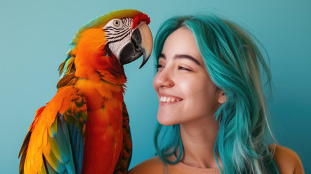 Young woman with vibrant blue hair smiling at colorful parrot against a blue background. Concepts of exotic pets, joyful companionship, and vivid colors.の素材