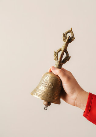 Hand ringing golden ceremonial bell on beige background during papal conclave announcement.の写真素材