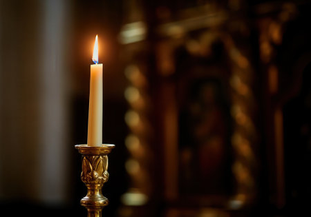 Elegant lit candle in golden holder against blurred dark background.の写真素材