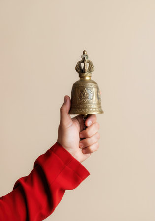 Hand holding ornate brass bell with crown design on beige background.の写真素材