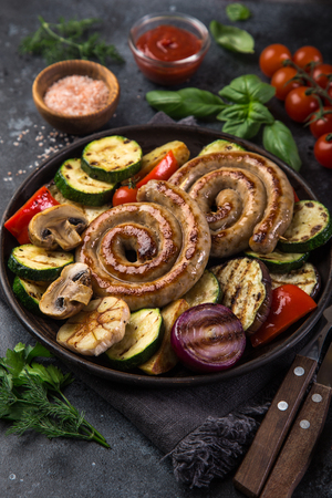 grilled spiral sausages and vegetables on dark plate, selective focusの写真素材