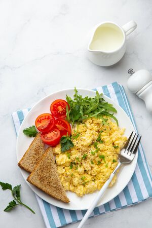 scrambled eggs, tomatoes, toasted bread and greens  for breakfast, white table, top viewの写真素材