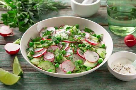 Fresh radish, cucumber and green peas salad in white bowl, selective focusの写真素材