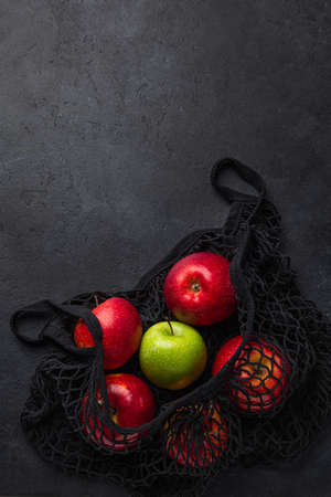 Fresh organic apples in black reusable textile shopping bag. Zero waste and eco-friendly concept. Black background, top view, copy spaceの写真素材