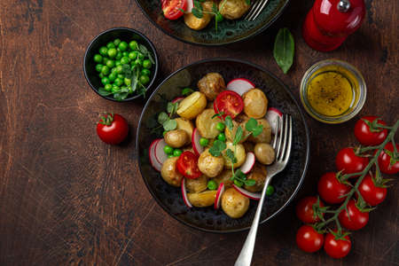 baby potatoes salad with tomato, green peas and radish, wooden background, top viewの写真素材