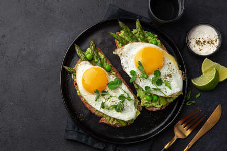 toasts with avocado, asparagus and fried egg on black plate, top view, dark background, copy spaceの写真素材