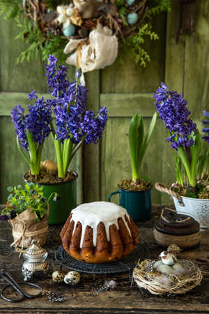 Easter bread with sugar glaze and dried fruits, dark rustic background with vintage Easter decoration and spring hiacinth flowersの写真素材
