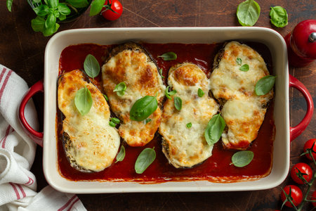 cheesy stuffed eggplant parmigiana with tomato sauce in baking dish, top view, wooden background
