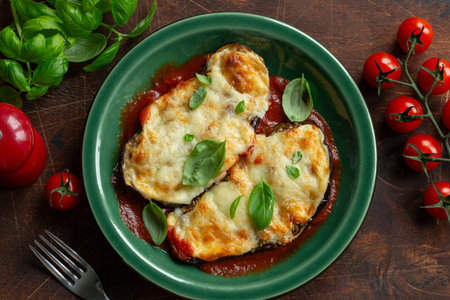 cheesy stuffed eggplant parmigiana with tomato sauce on green plate, top view, wooden background