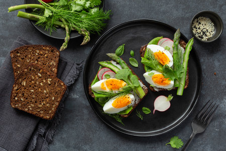 toast with dark rye bread asparagus and soft boiled egg on black plate, top viewの写真素材
