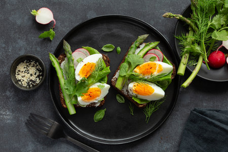 sandwich with dark rye bread, asparagus and soft boiled egg, black plate, top viewの写真素材