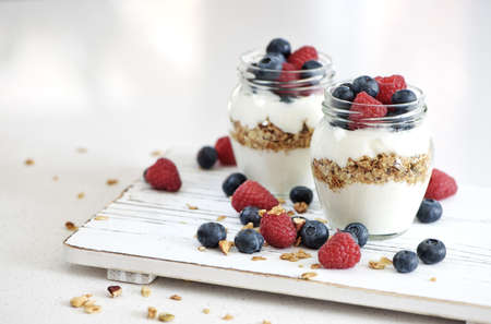 Yogurt with bluberry and raspberry in the glass jars with berries around on the wooden boardのeditorial素材
