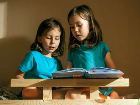 A girl reads a book for the night of her younger sisterの写真素材