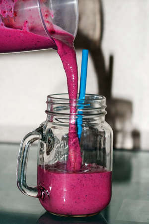 Berry smoothies from milk, blueberries and currants are poured into a transparent mug with a strawの写真素材