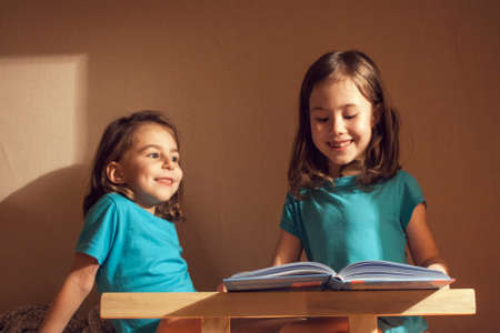 A girl reads a book for the night of her younger sisterの写真素材