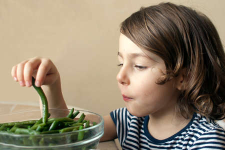 A small child is eating a fresh string bean